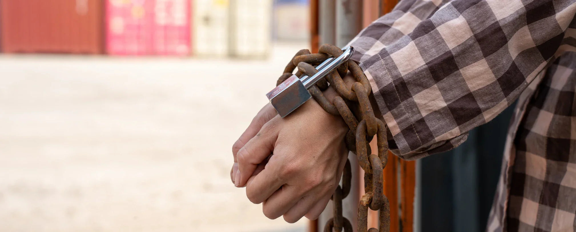 close-up of a person's wrists wrapped in heavy rusted chains secured with a padlock