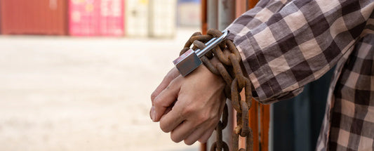 close-up of a person's wrists wrapped in heavy rusted chains secured with a padlock
