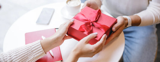 woman in office handing over a gift in red box and bow reposted by Made for Freedom