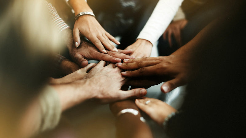 Diverse group of people joining hands together in a circle to symbolize unity, support, and community action.