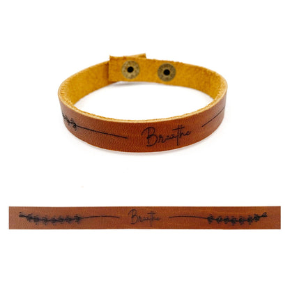 A tan leather bracelet with a yellow inner lining and black engraved text reading 'Breathe', shown on a white background with a flat detail view of the engraving below.