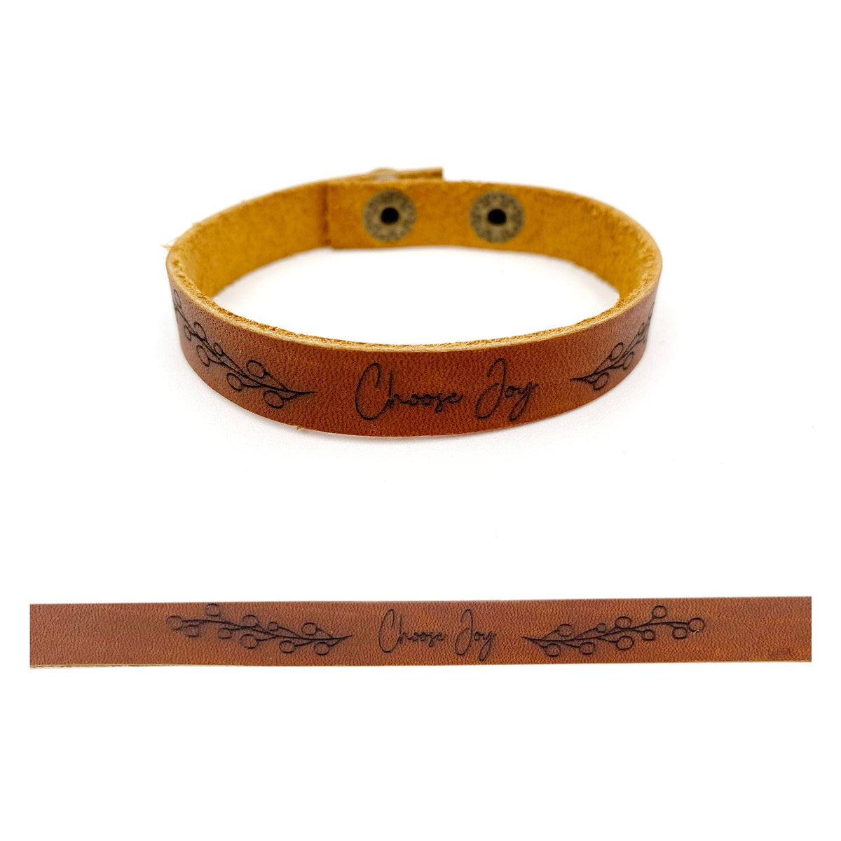A tan leather bracelet with black decorative scrollwork and the words 'Choose Joy' printed on it, shown on a white background with a flat close-up strip below.