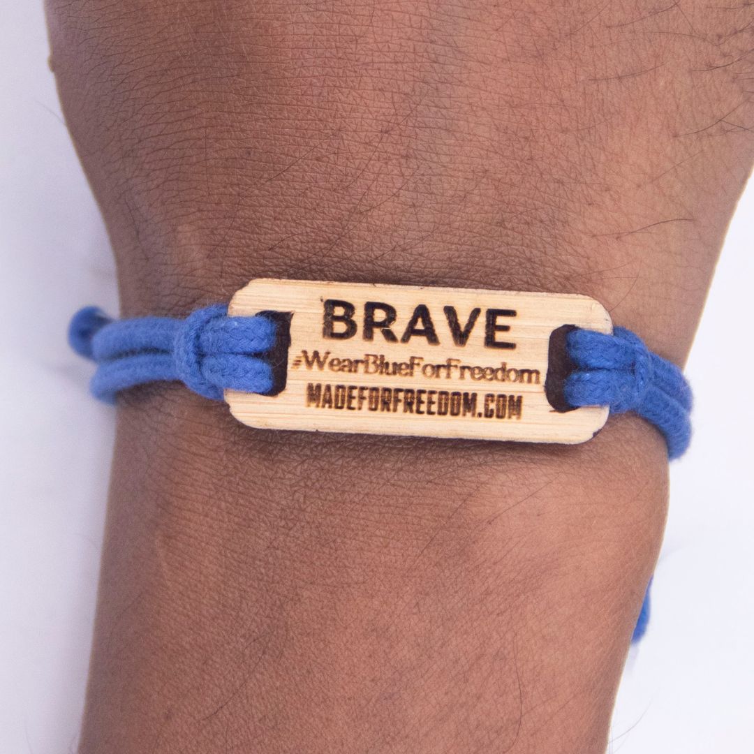 Bracelet with wooden tag labeled 'BRAVE' on a wrist, featuring branding text.