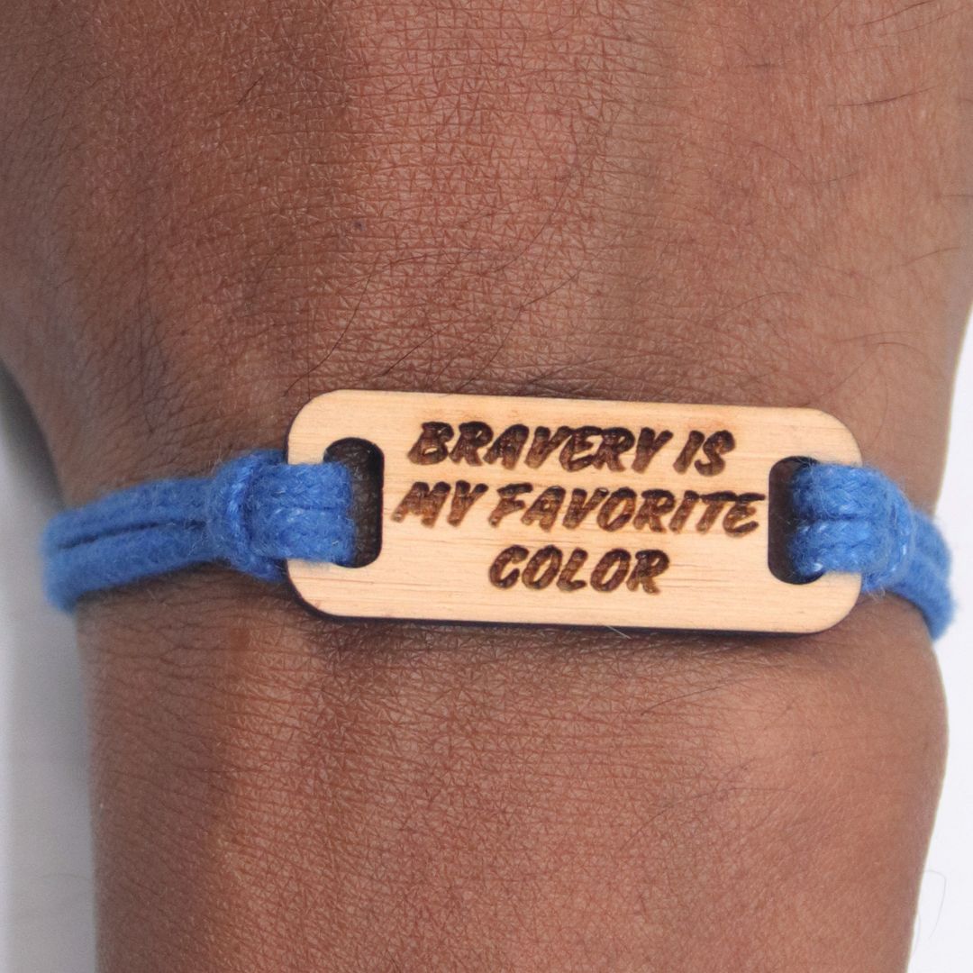 Bracelet with wooden tag reading 'Bravery is my favorite color' on a wrist.