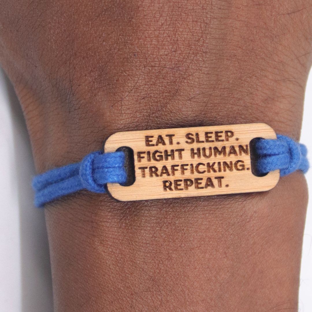 Bracelet with wooden tag reading 'Eat. Sleep. Fight Human Trafficking. Repeat.' on a wrist.
